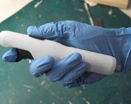 Photograph of a gloved hand holding a foam model of a white medical device.